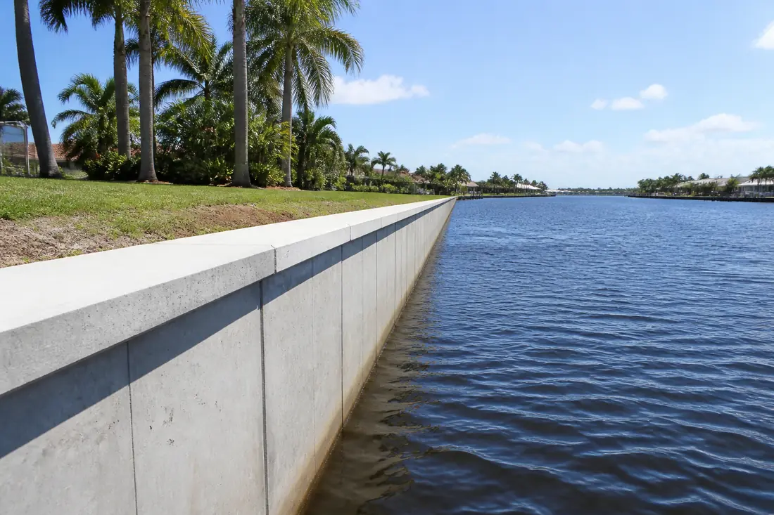 A concrete seawall running along a Cape Coral canal with open water beyond