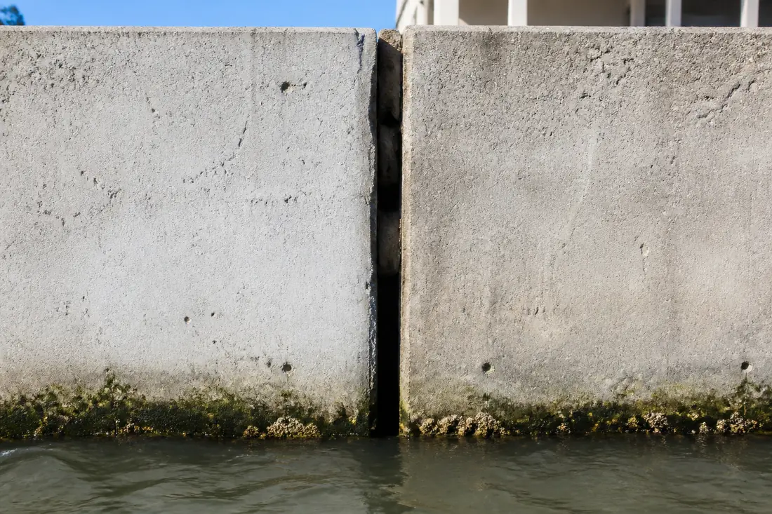 An open vertical joint between two concrete seawall panels with soil visible in the gap